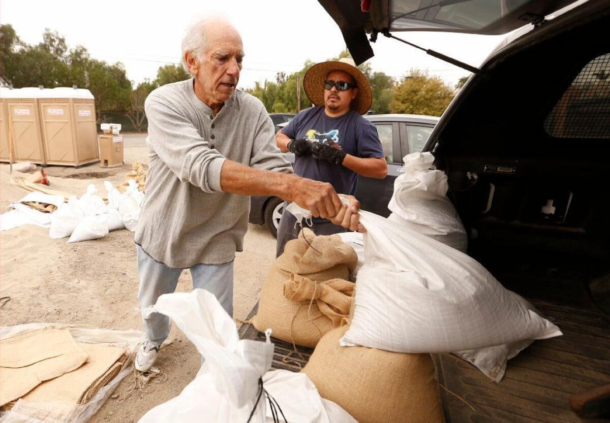 Victor Lobl loads sandbags provided by the L.A. County Fire Department on Monday with the help of friends to protect what's left of his Malibu home.
