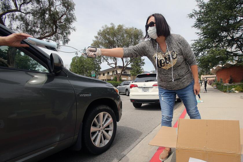 Caroline Anderson, of La Canada Flintridge, uses grilling tongs to hand a packet of 10 masks to a person in her drive-through station for the Masks for Many program by the Chinese Club of La Canada and La Crescenta at the Foothill Chinese School in La Canada Flintridge on Tuesday, March 31, 2020. The club has 30,000 masks to distribute, some today to a steady stream of cars, and some at Two Strike Park in La Crescenta on April 2 from 10:00 A.M. to 11:00 A.M.