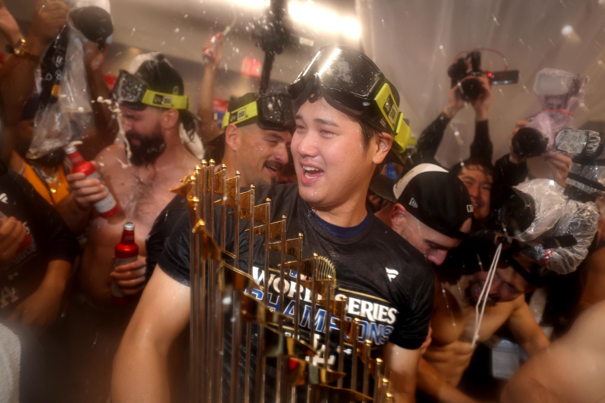 Dodgers star Shohei Ohtani holds the World Series trophy as he celebrates with teammates in the locker room.