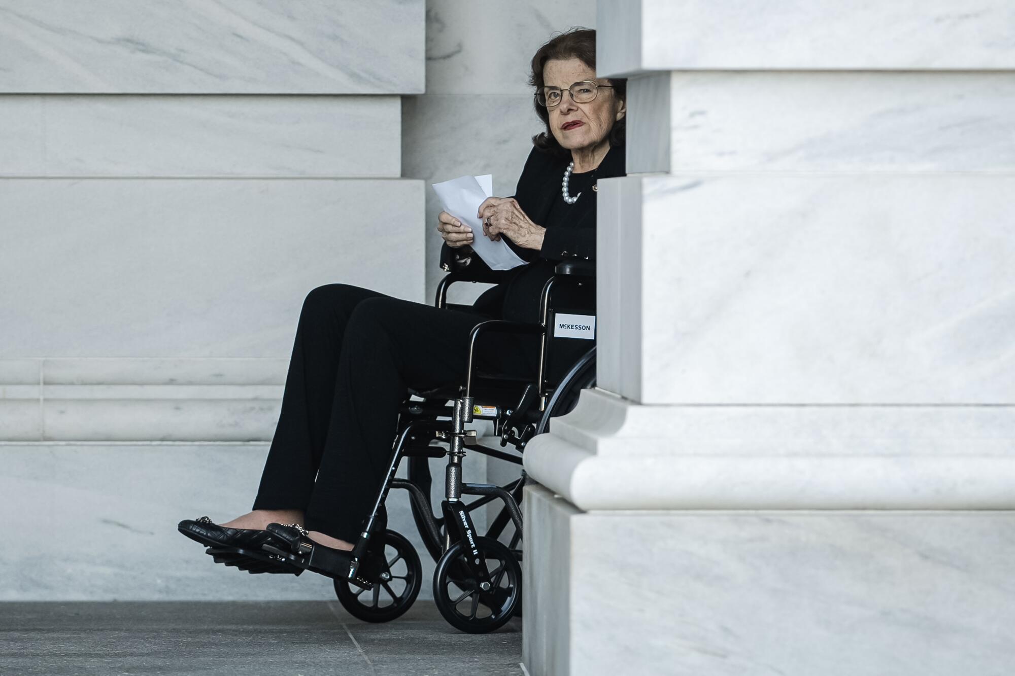 A person in a wheelchair appears behind a marble column.