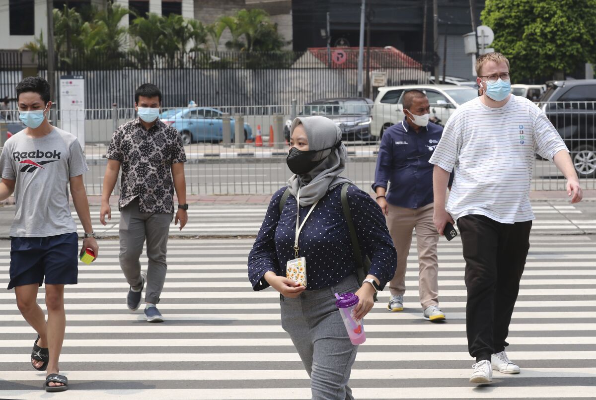 People wearing face masks as a precaution against the new coronavirus outbreak, walk along a pedestrian crossing in the main business district in Jakarta, Indonesia, Thursday, Dec. 16, 2021. The Indonesian government on Thursday announced that the country has detected its first case of omicron variant on Wednesday evening. (AP Photo/Tatan Syuflana)