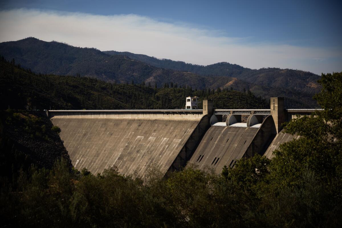 Shasta Dam with mountains and clouds, blue sky in the background.