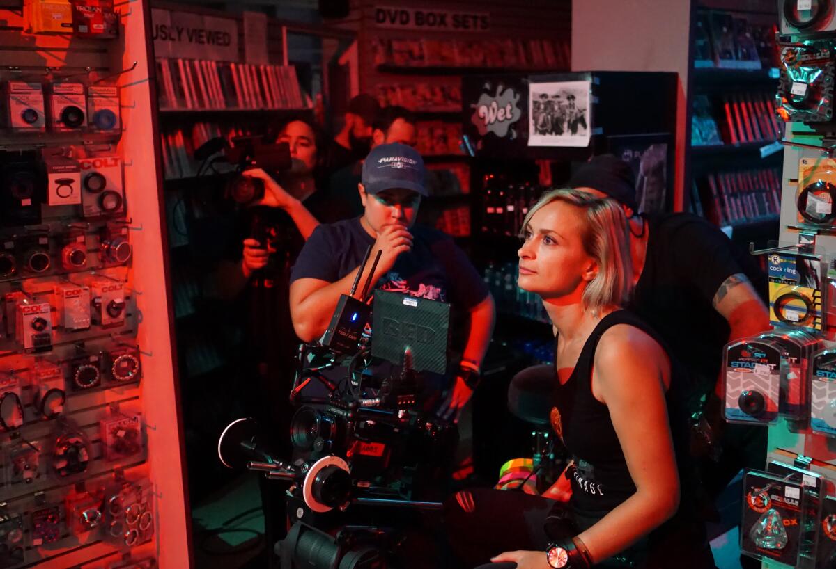 A woman with a movie camera rig on the set, with other crew members in the background