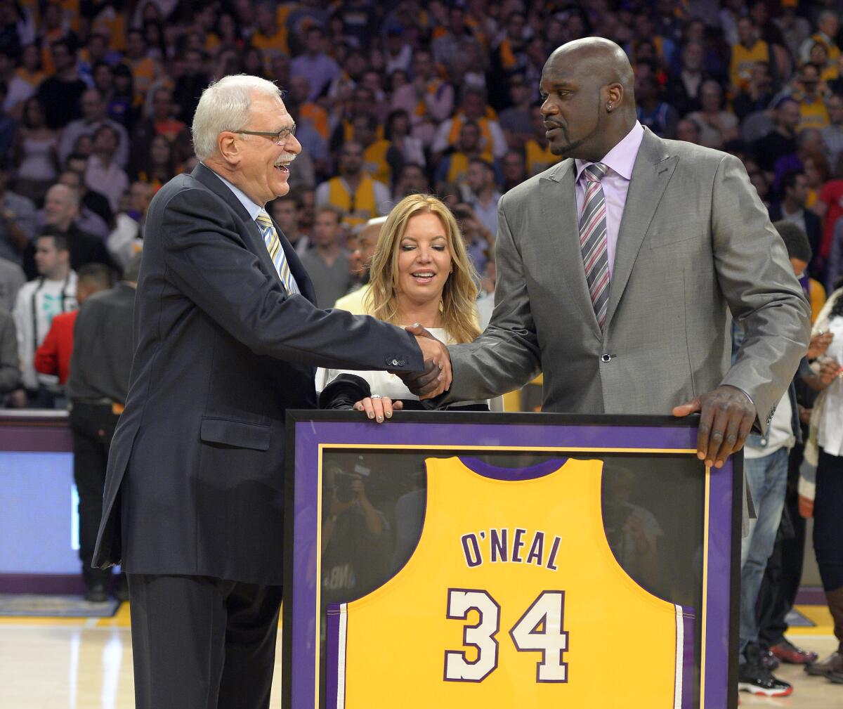 Former Lakers center Shaquille O'Neal, right, shakes hands with former Lakers coach Phil Jackson in front of a framed jersey.