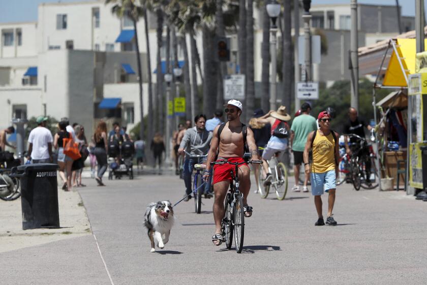 A bicyclist cruises as he walks his dog along the bike path on the north side of Huntington Beach Pier on Friday, April 24.