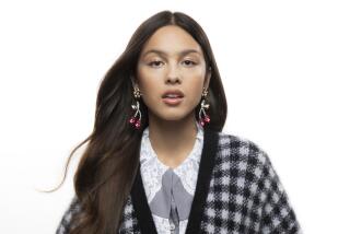 Olivia Rodrigo posing in a checkered sweater and cherry earrings