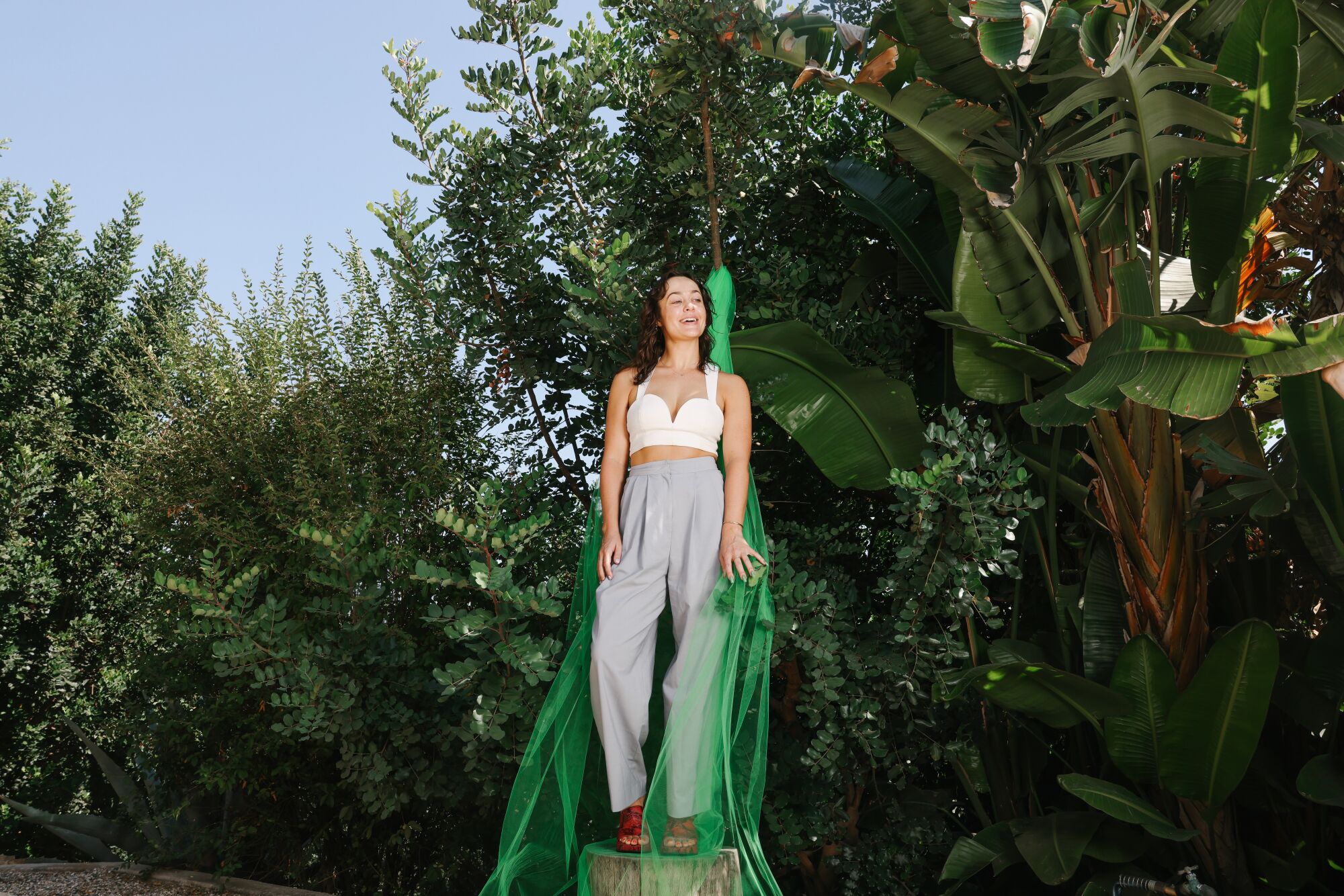 Alyssa Nader standing on a tree stump with plants and a green piece of tulle behind her.