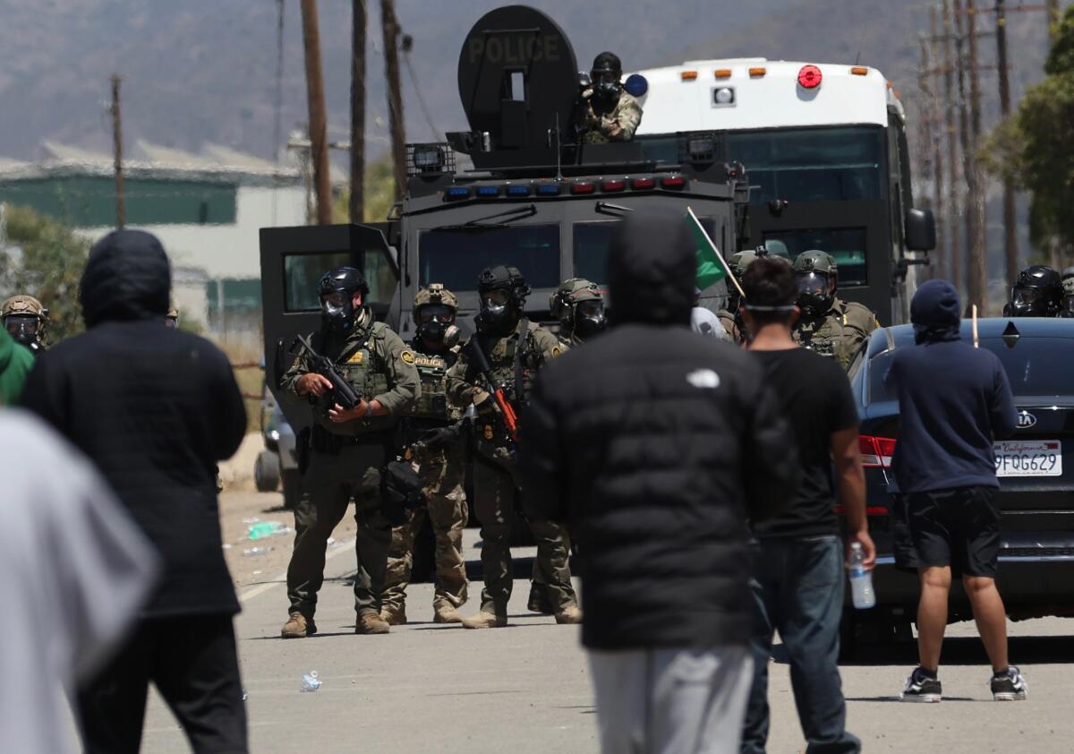 Federal officers hold a line against protesters opposing immigration enforcement along Laguna Road