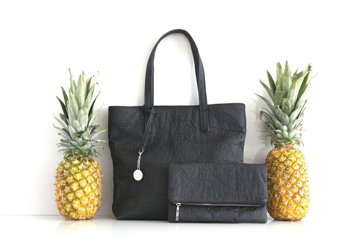 Two pineapples next to a black tote and a black clutch.