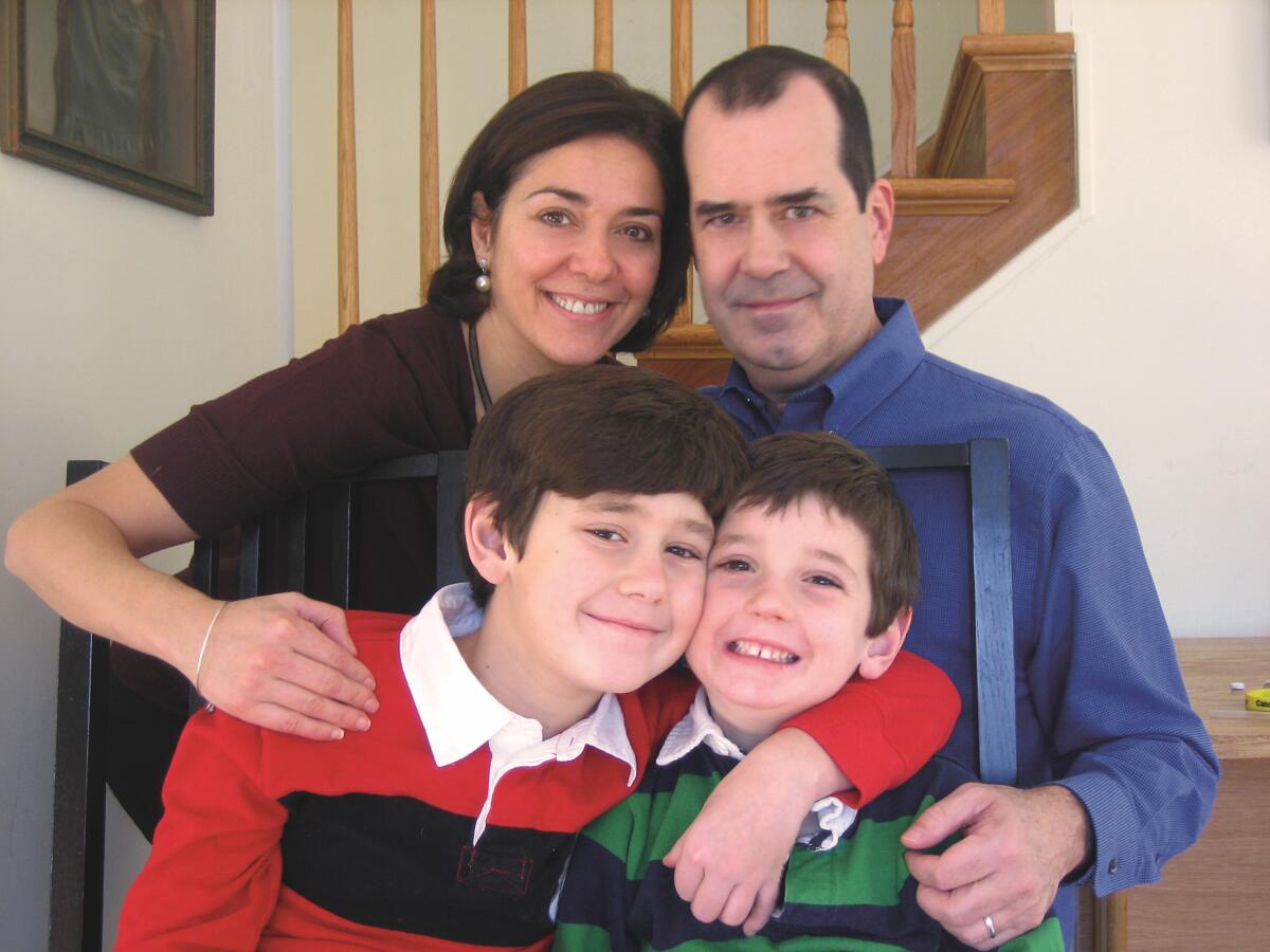 Bir erkek, bir kadın ve iki erkek çocuktan oluşan dört kişilik bir aile, oturma odalarında fotoğraf çektirmek için gülümsüyor.