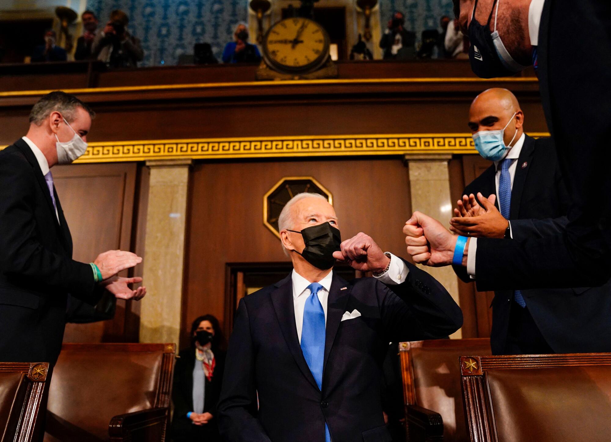 President Biden, in a face mask, bumps arms with another man.