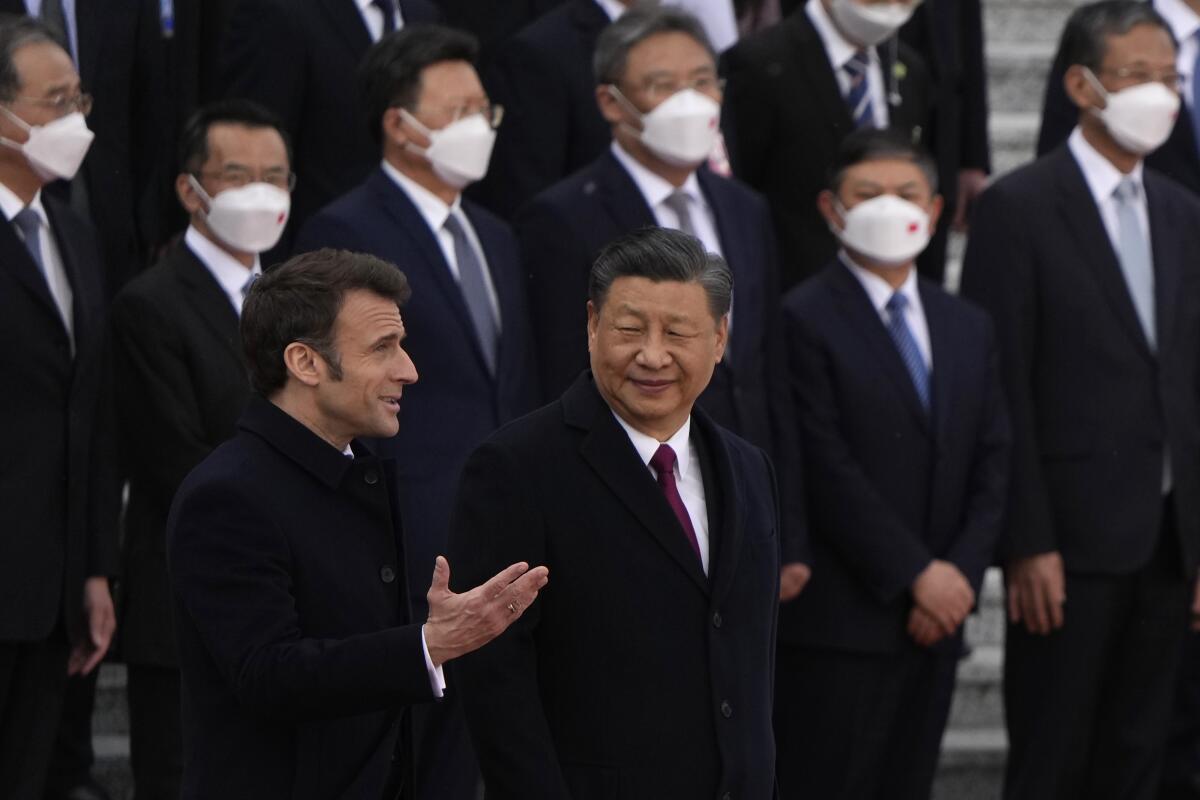 French President Emmanuel Macron and Chinese President Xi Jinping at welcome ceremony where other men stand behind them.
