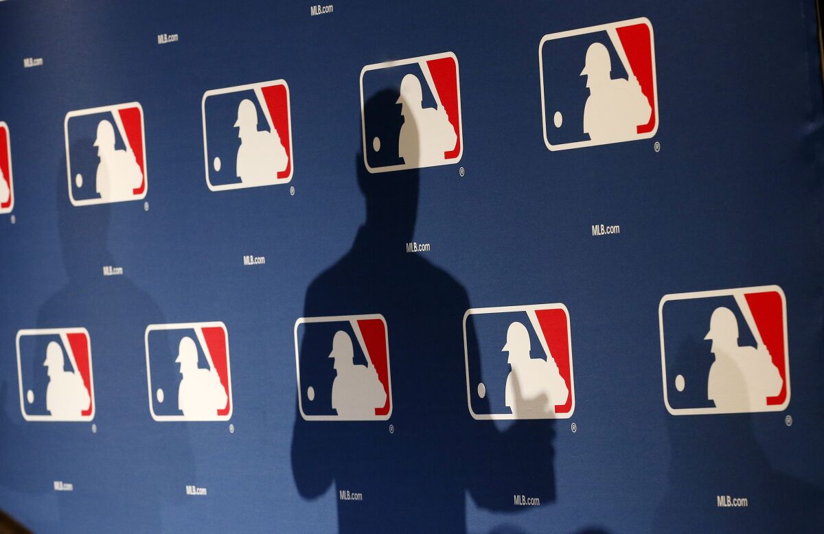 The shadow of MLB commissioner Rob Manfred is projected on an MLB logo backdrop.