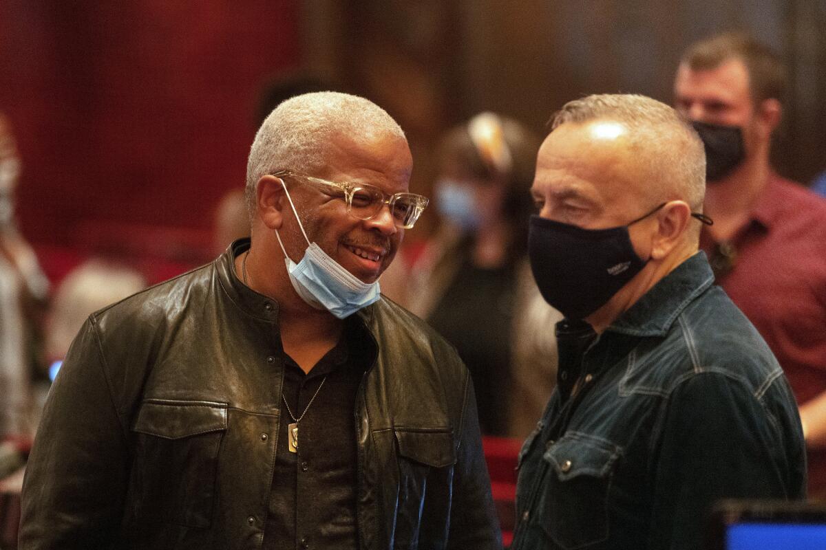 Terence Blanchard, a mask around his chin, talks to James Robinson in a rehearsal space.