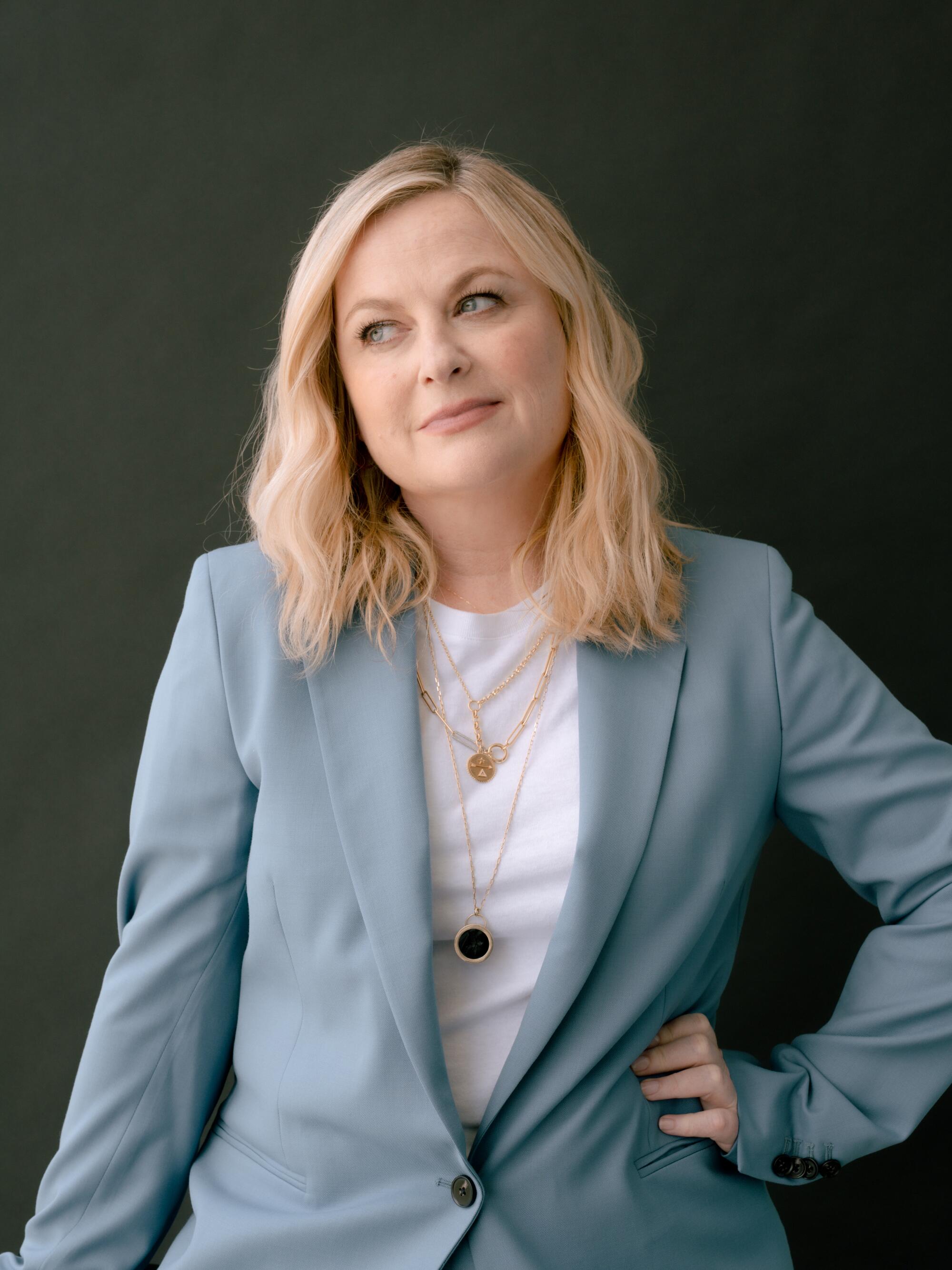 A woman in a light blue suit sits for a portrait against a dark green background