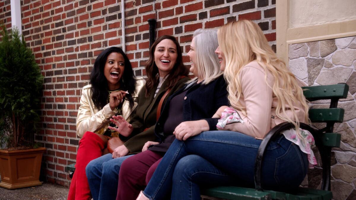Four women laughing and talking on a bench