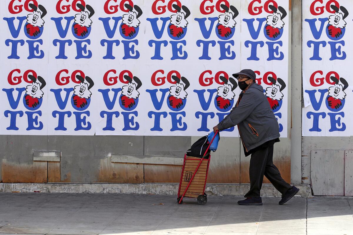 A man walks on a city sidewalk past a wall covered with "Go Vote" signs.