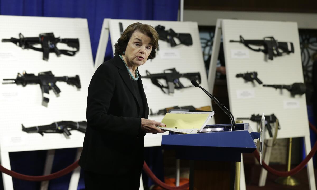 A woman stands in front of displays of guns.