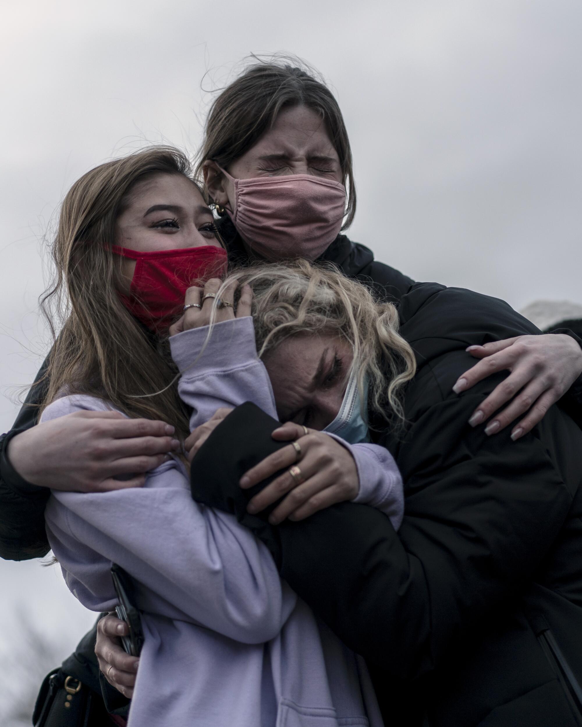 Three women embrace and mourn together while looking at the scene outside the King Soopers grocery store