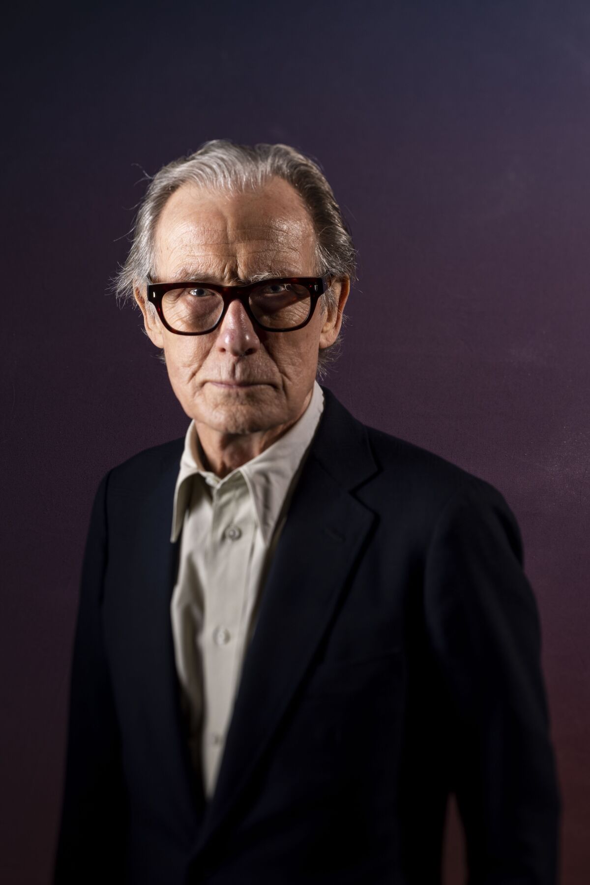 Bill Nighy wears a gray shirt and black jacket for a portrait.