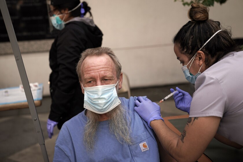 FILE - In this Feb. 3, 2021, file photo, EMT Rachel Bryant, right, administers a COVID-19 vaccine to a homeless man in the courtyard of the Midnight Mission in Los Angeles. Homeless Americans who have been left off priority lists for coronavirus vaccinations — or even bumped aside as states shifted eligibility to older age groups — are finally getting their shots as vaccine supplies increase. (AP Photo/Jae C. Hong)