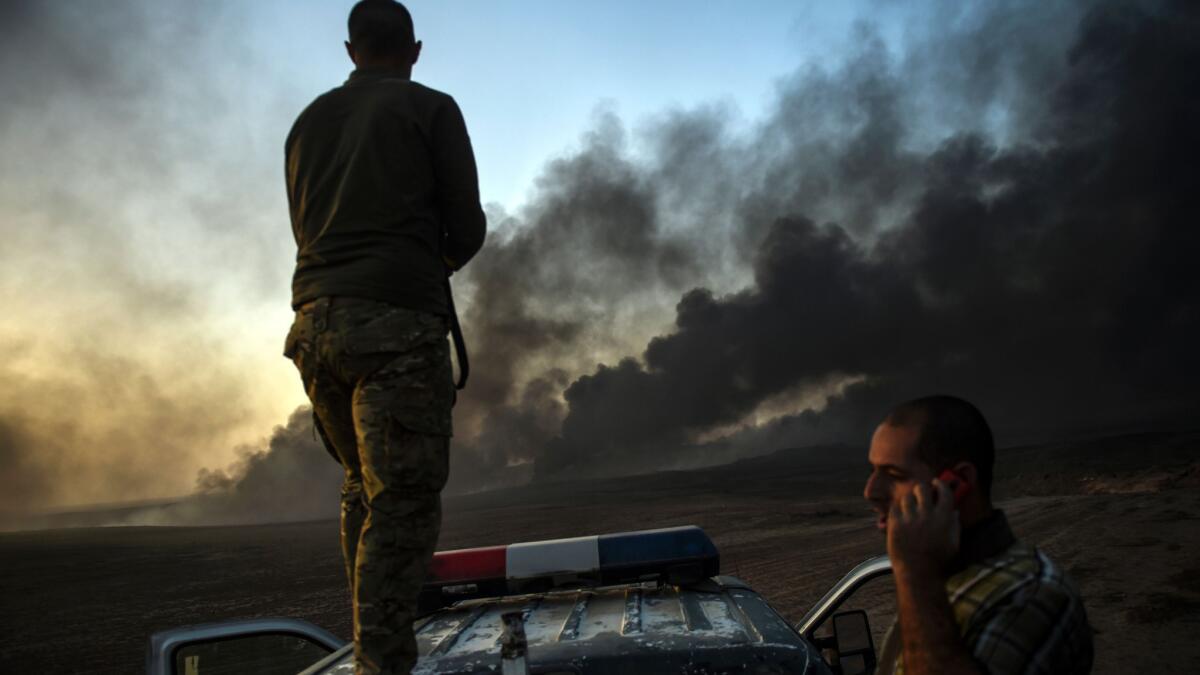 An Iraqi fighter takes position on top of vehicle as smoke rises from the outskirts of Qayyarah, south of Mosul.