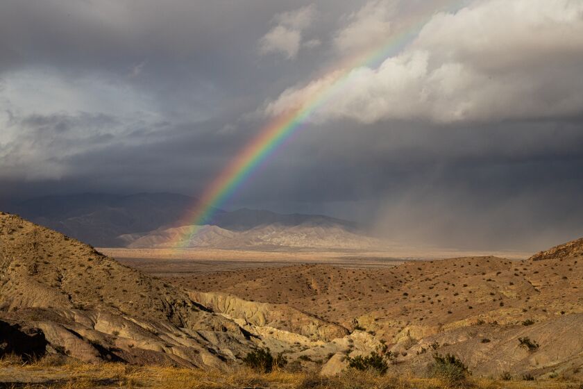 A desert rainbow looks out over the Borrego Badlands with winds stirring up a dust storm on the right.