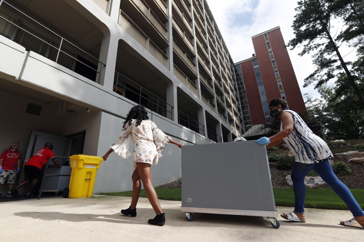 Two women wheel a large cart toward a college dorm.