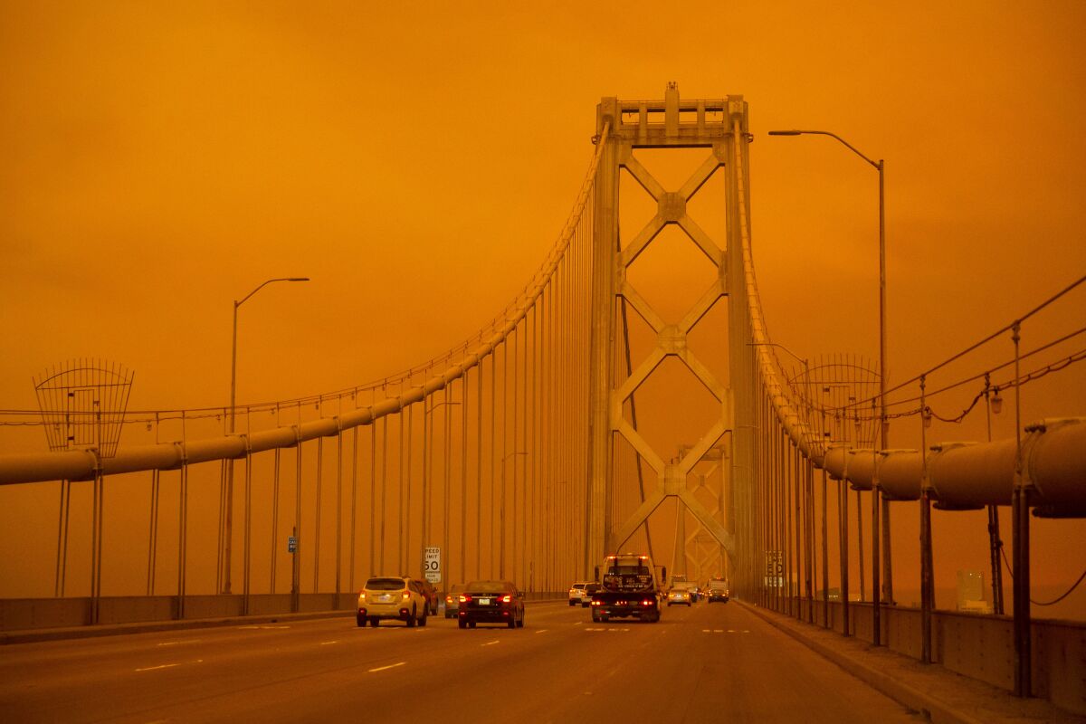 Cars drive along the San Francisco Bay Bridge under an orange smoke-filled sky