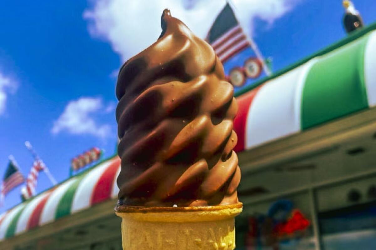 A swirling chocolate soft-serve ice cream cone outside a shop with a red white and green awning