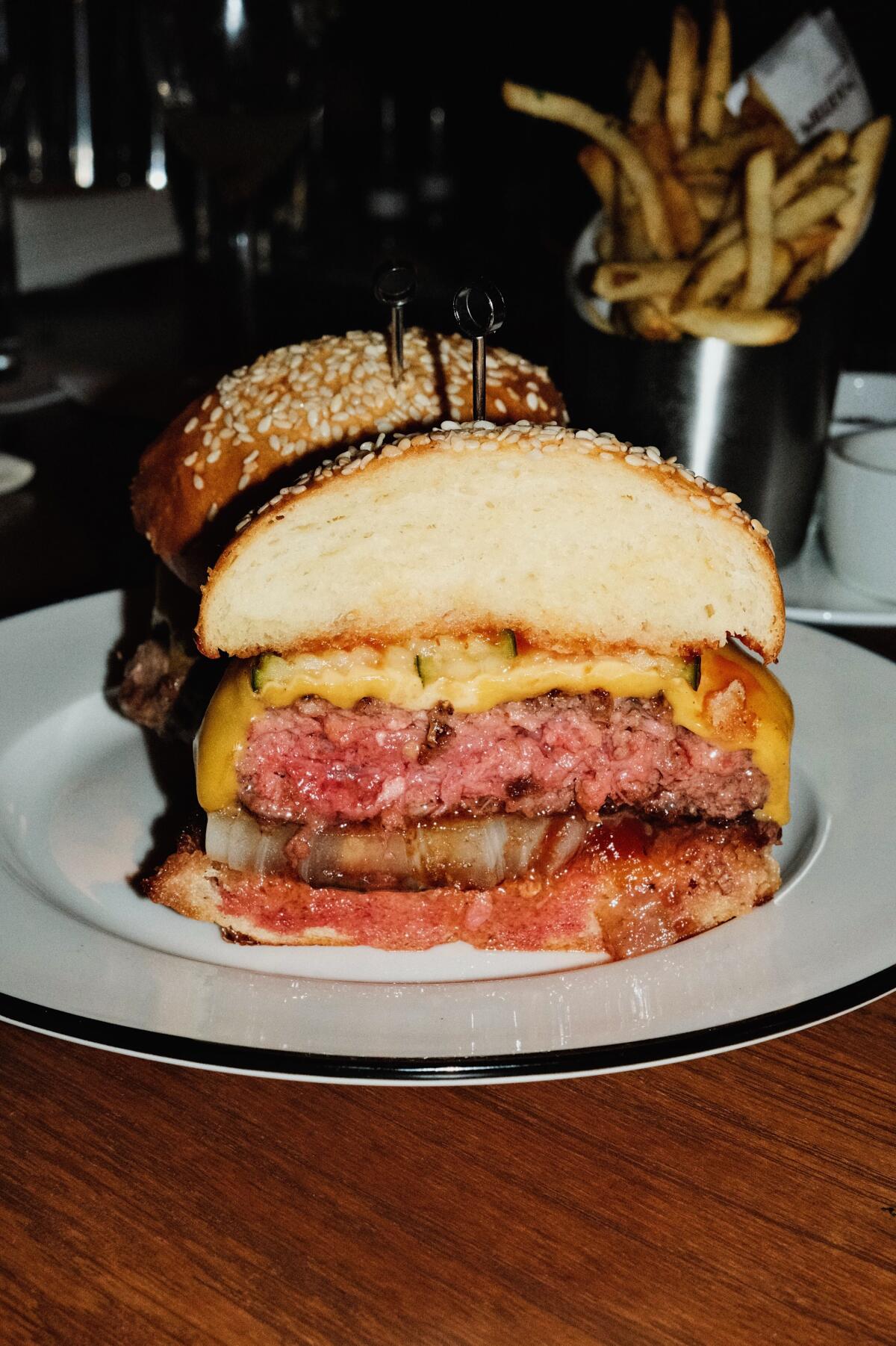 The cheeseburger at the Benjamin, cut in half, on a white plate. French fries are seen in the background.