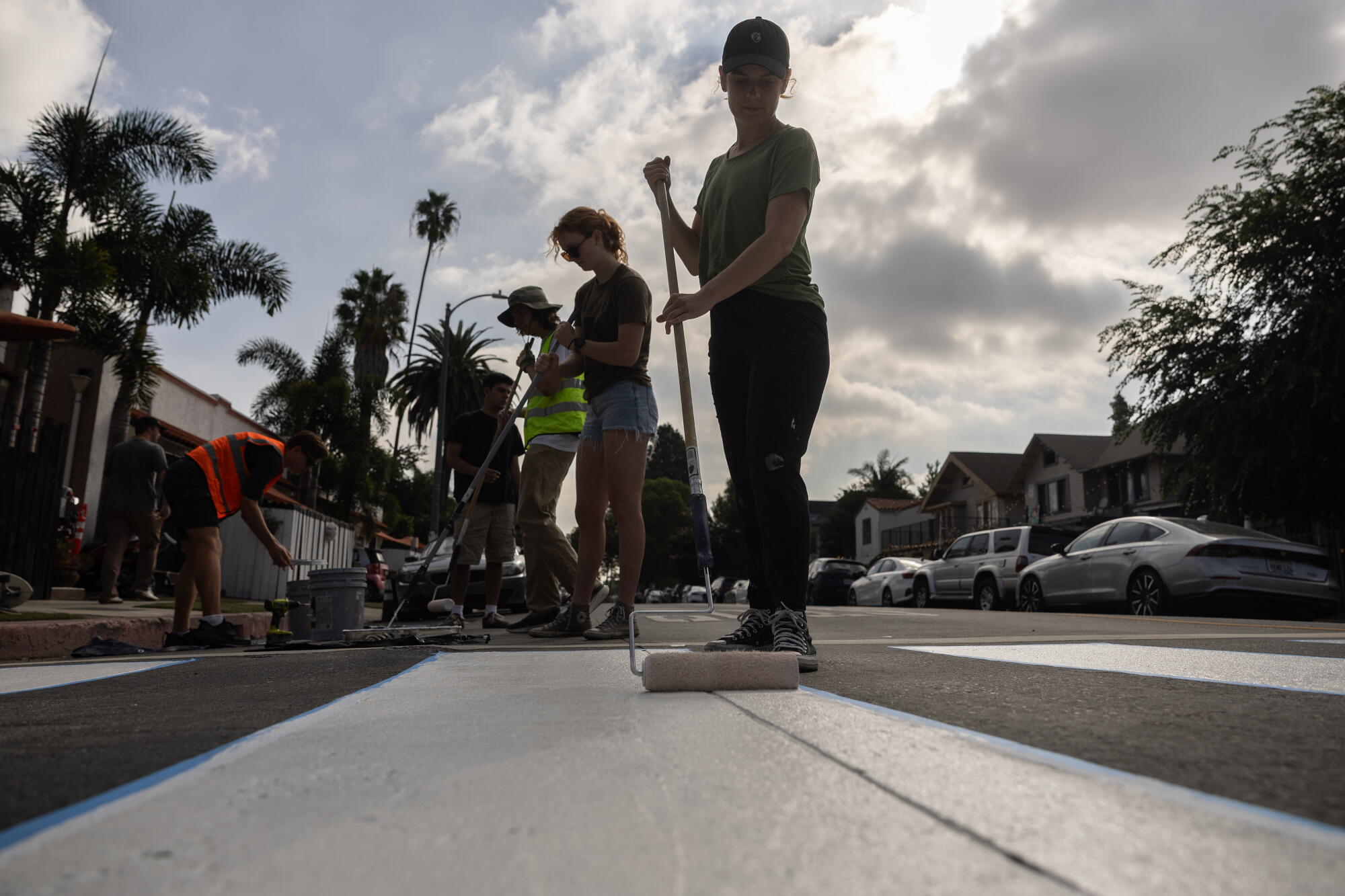 A female uses a agelong roller brushwood to overgarment a achromatic stripe connected a street.