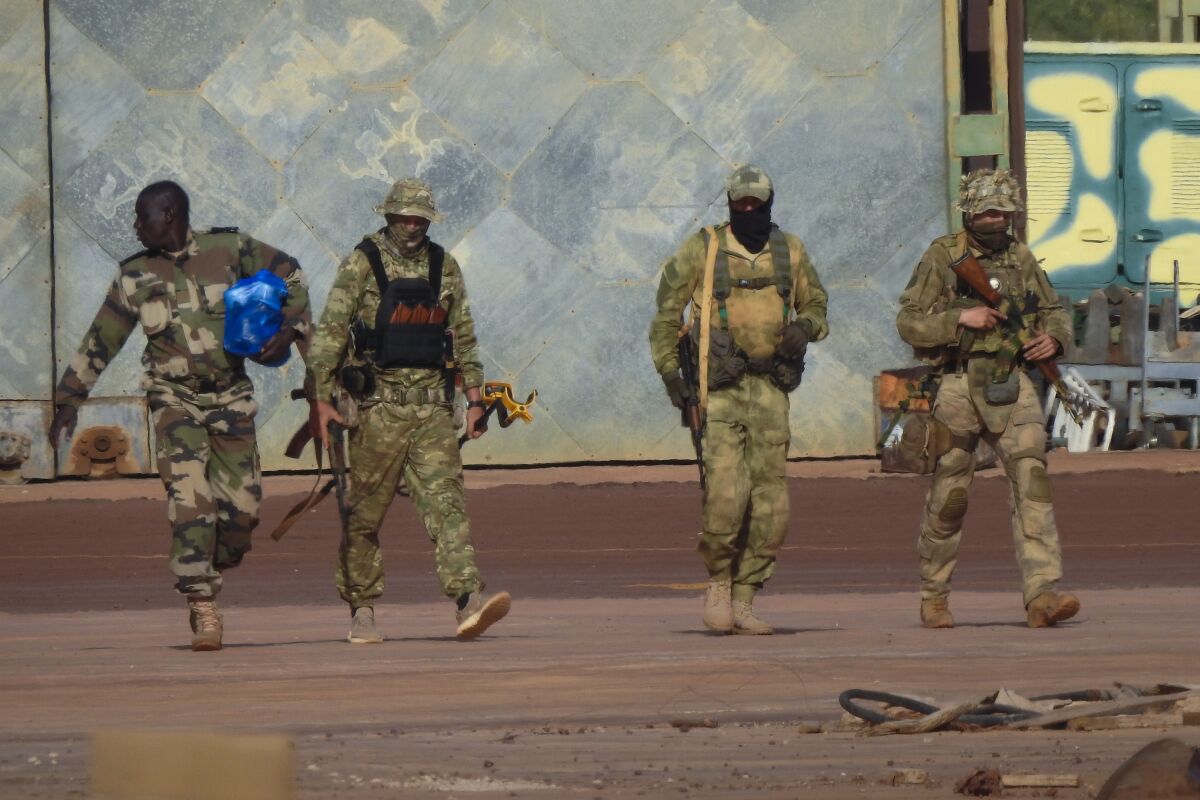 Three Russian mercenaries and a fourth armed person in camouflage walking 