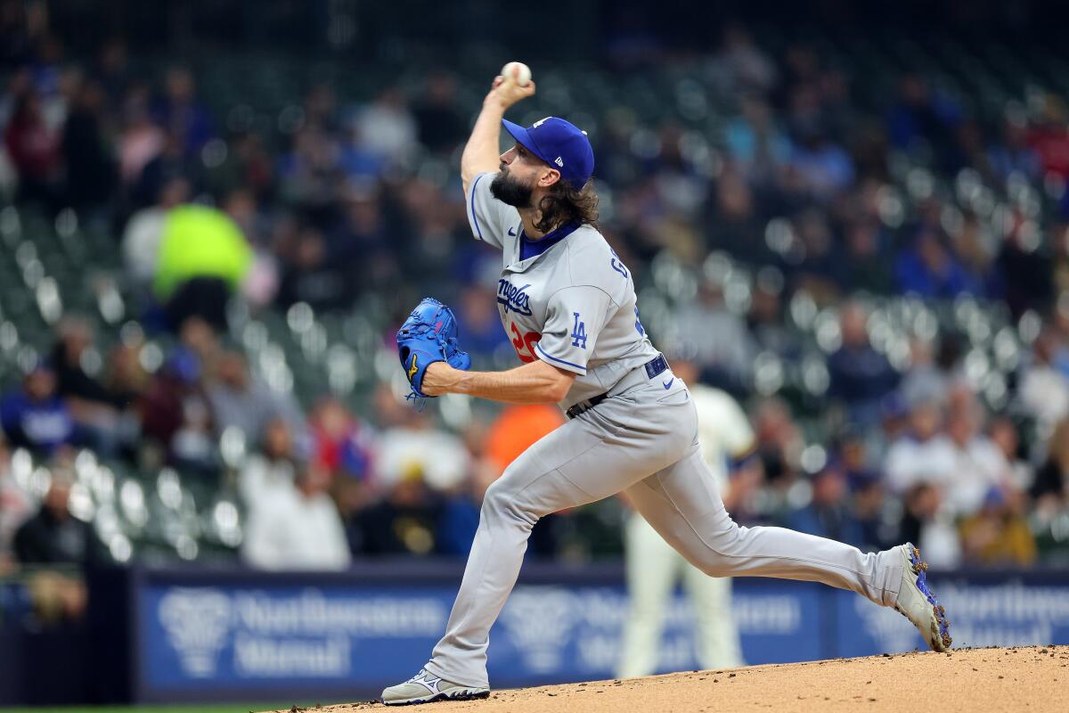 A man in a blue hat and gray uniform lifts his arm while holding a baseball and leaning into a throw.