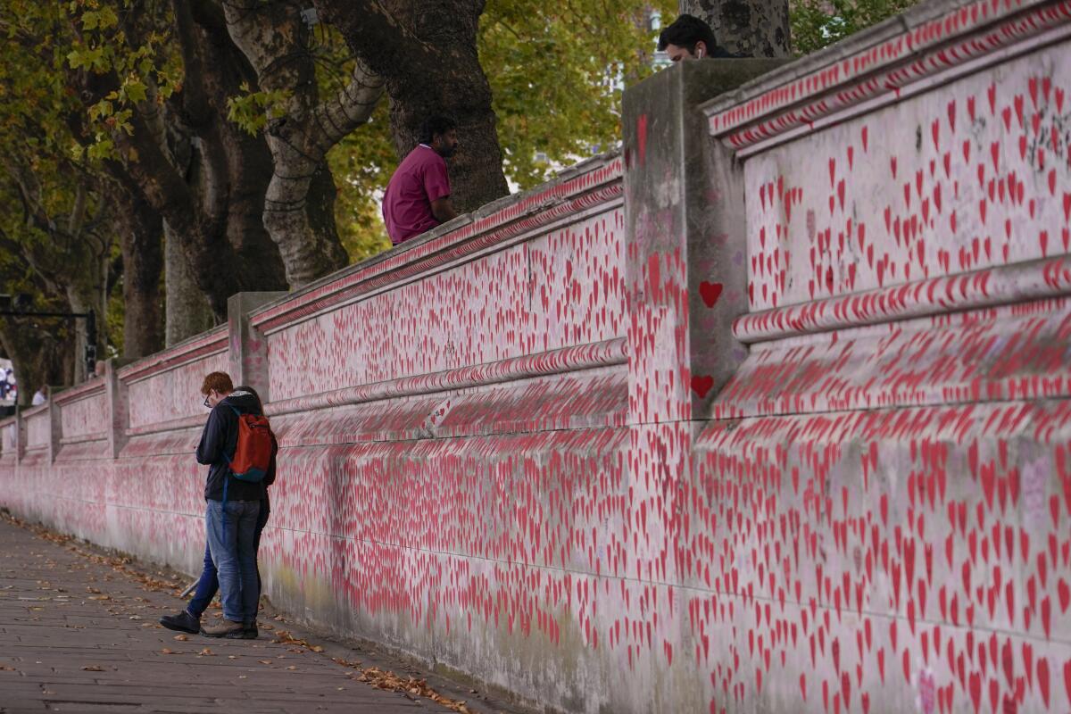 A person in a backpack stands alongside a wall covered with small red hand-painted hearts.