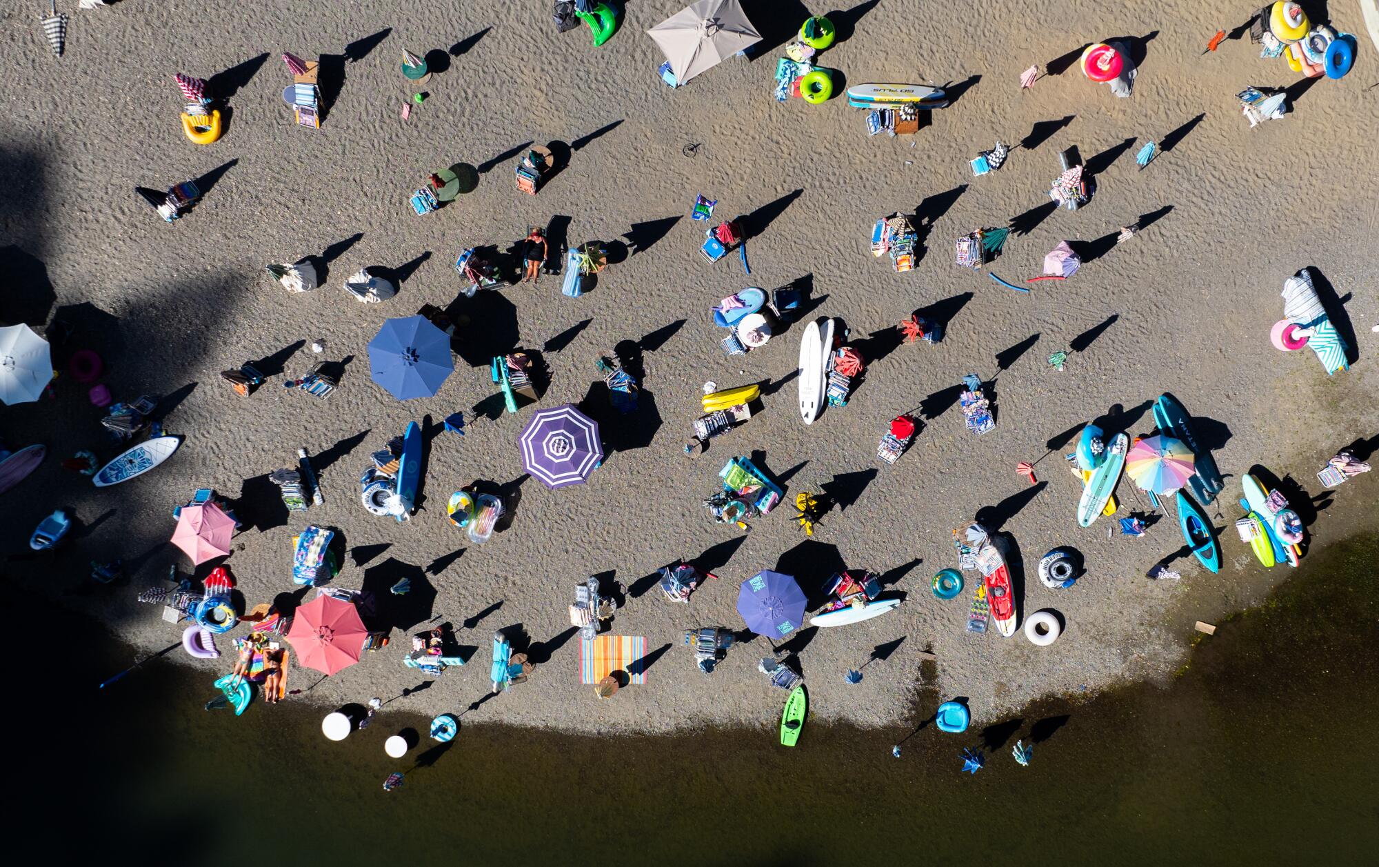 An aerial view of umbrellas, inner tubes and water toys sitting idle on a beach devoid of people.