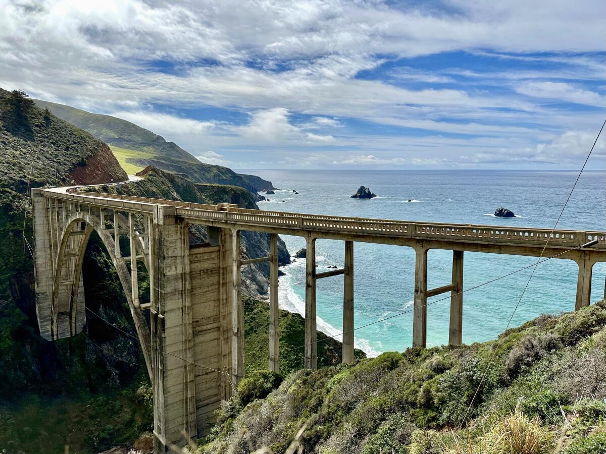 A large concrete bridge in mountains on the rocky coastline, with the ocean in the background.