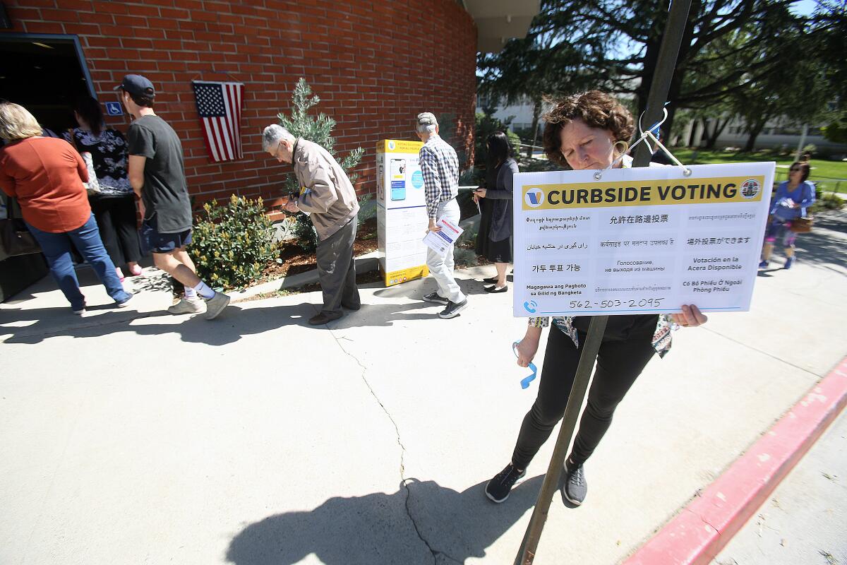 Poll worker Samela Beasom, of La Cañada, tries to secure a curbside voting sign onto a post as voters queue up at the La Cañada Unified School District on Election Day, March 3. Some voters reported wait times of up to 90 minutes.