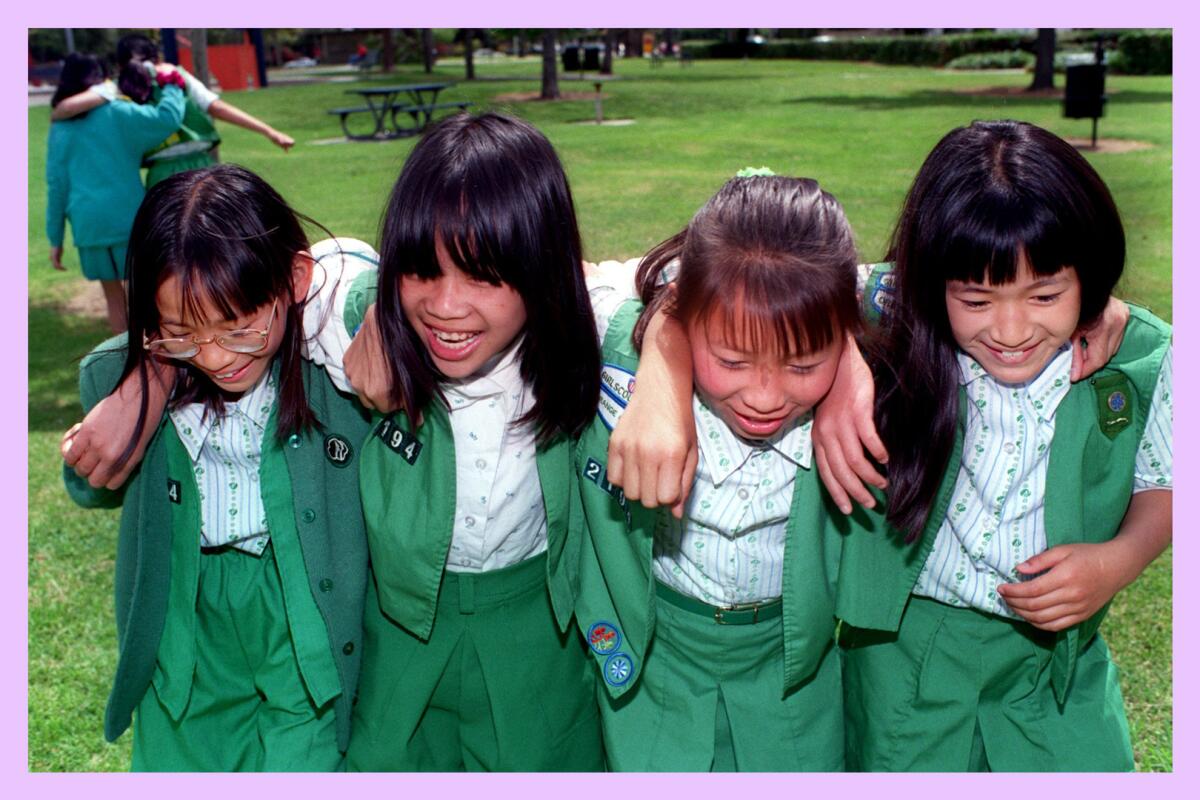 Four Girl Scouts wearing uniforms stand with their arms around each other.