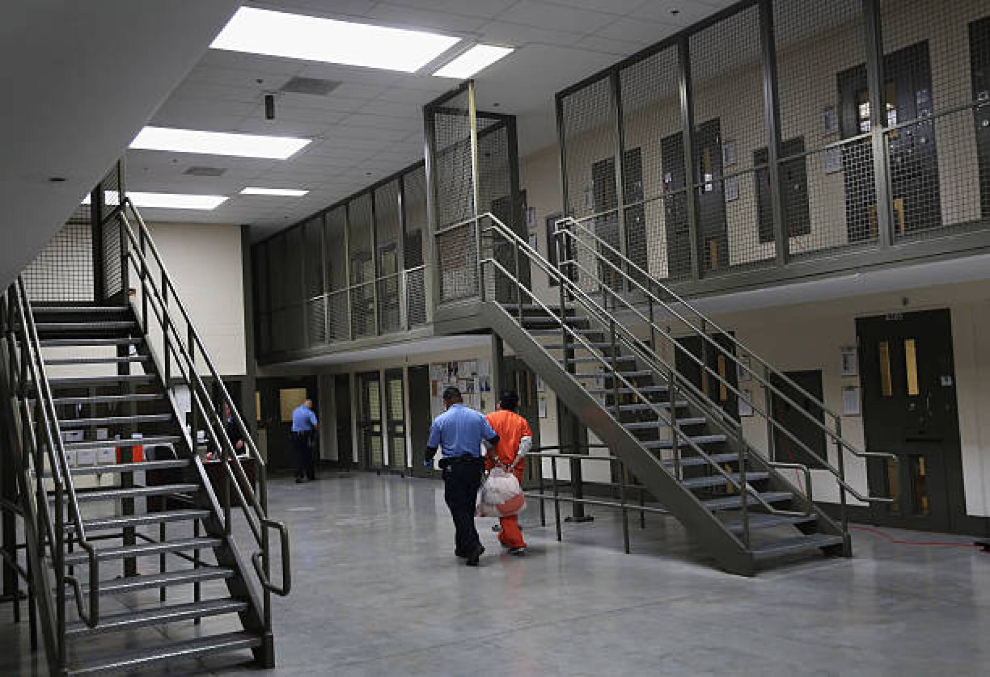 A guard in uniform, left, walks with an immigrant detainee in an orange suit