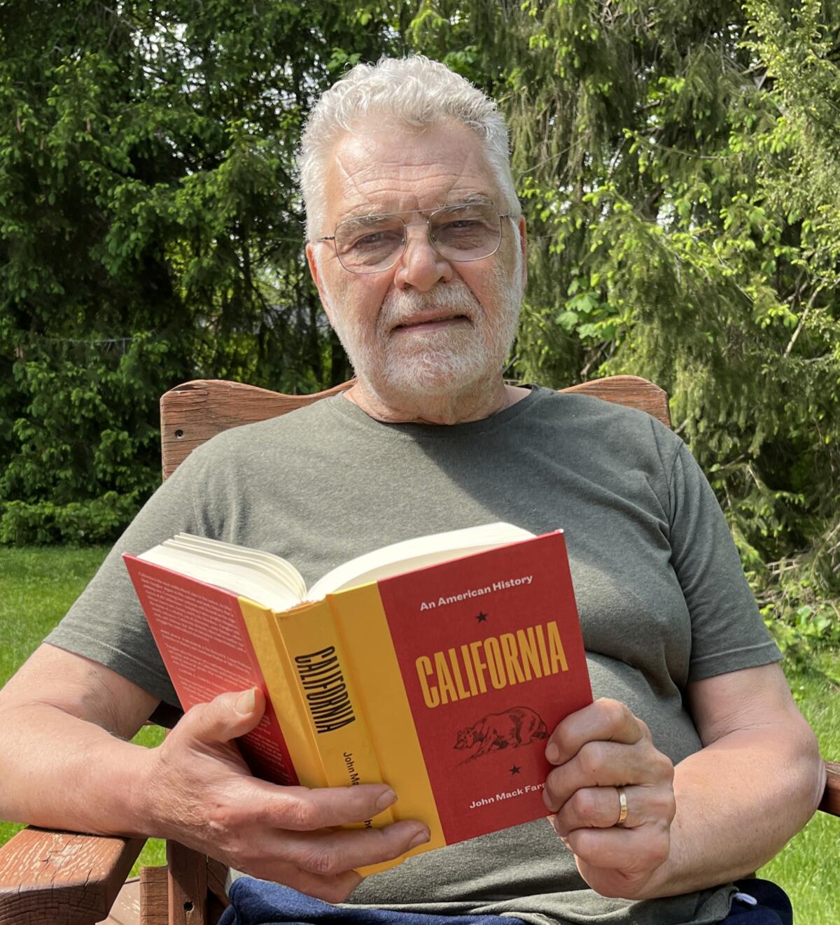 A man in a T-shirt sits outside holding a book open