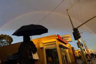Los Angeles, CA - January 03: A woman walks with an umbrella along Manchester Ave. amid rain as a double rainbow forms and a winter storm moves into Southern California in Los Angeles Wednesday, Jan. 3, 2024. (Allen J. Schaben / Los Angeles Times)