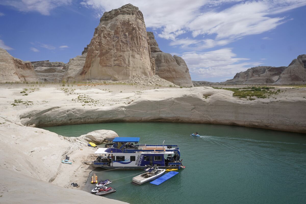 FILE - In this Friday, July 30, 2021 file photo, a houseboat rests in a cove at Lake Powell near Page, Ariz. This summer, the water levels hit a historic low amid a climate change-fueled megadrought engulfing the U.S. West. Severe drought across the West drained reservoirs this year, slashing hydropower production and further stressing the region’s power grids. And as extreme weather becomes more common with climate change, grid operators are adapting to swings in hydropower generation. (AP Photo/Rick Bowmer)