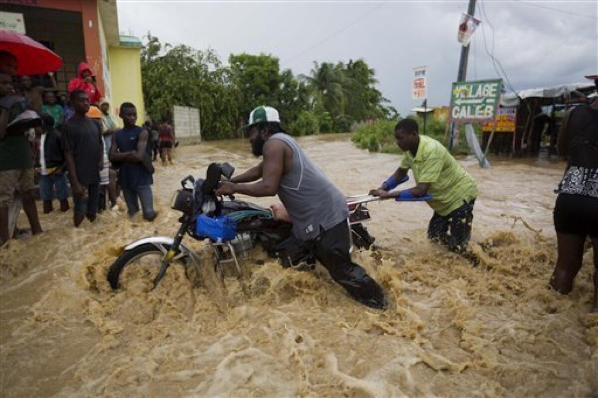 Dos hombres empujan una moto por una calle inundada por un río cercano, desbordado por las fuertes lluvias del huracán Matthew, en Leogane, Haití, el miércoles 5 de octubre de 2016. ( AP Foto/Dieu Nalio Chery)
