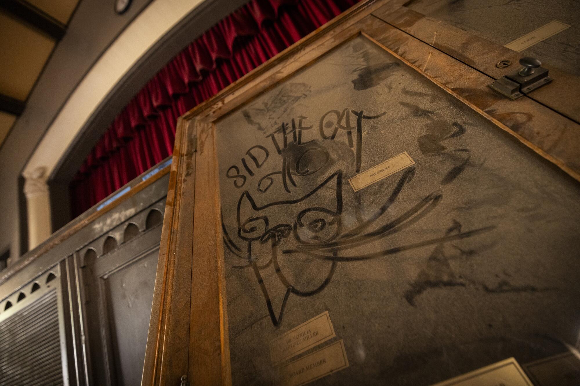 "Sid the Cat" over a cat's head in the dust covering an old glass panel.