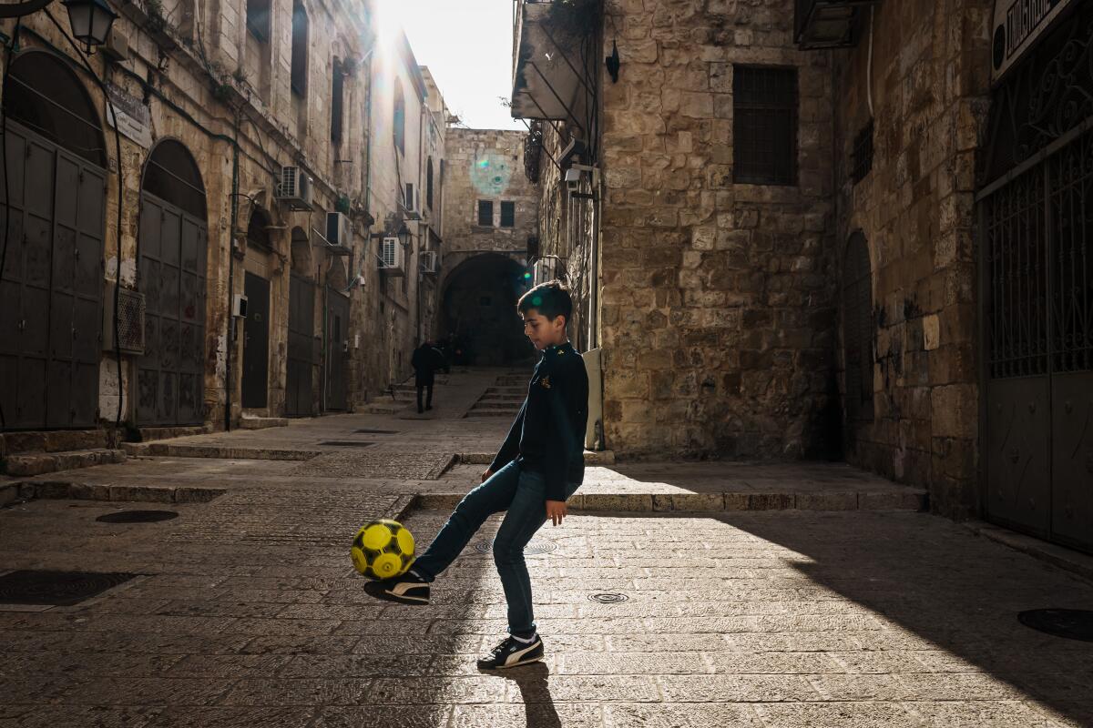یک پسر جوان فلسطینی در حال بازی با توپ فوتبال در محله مسلمانان در شهر قدیمی اورشلیم