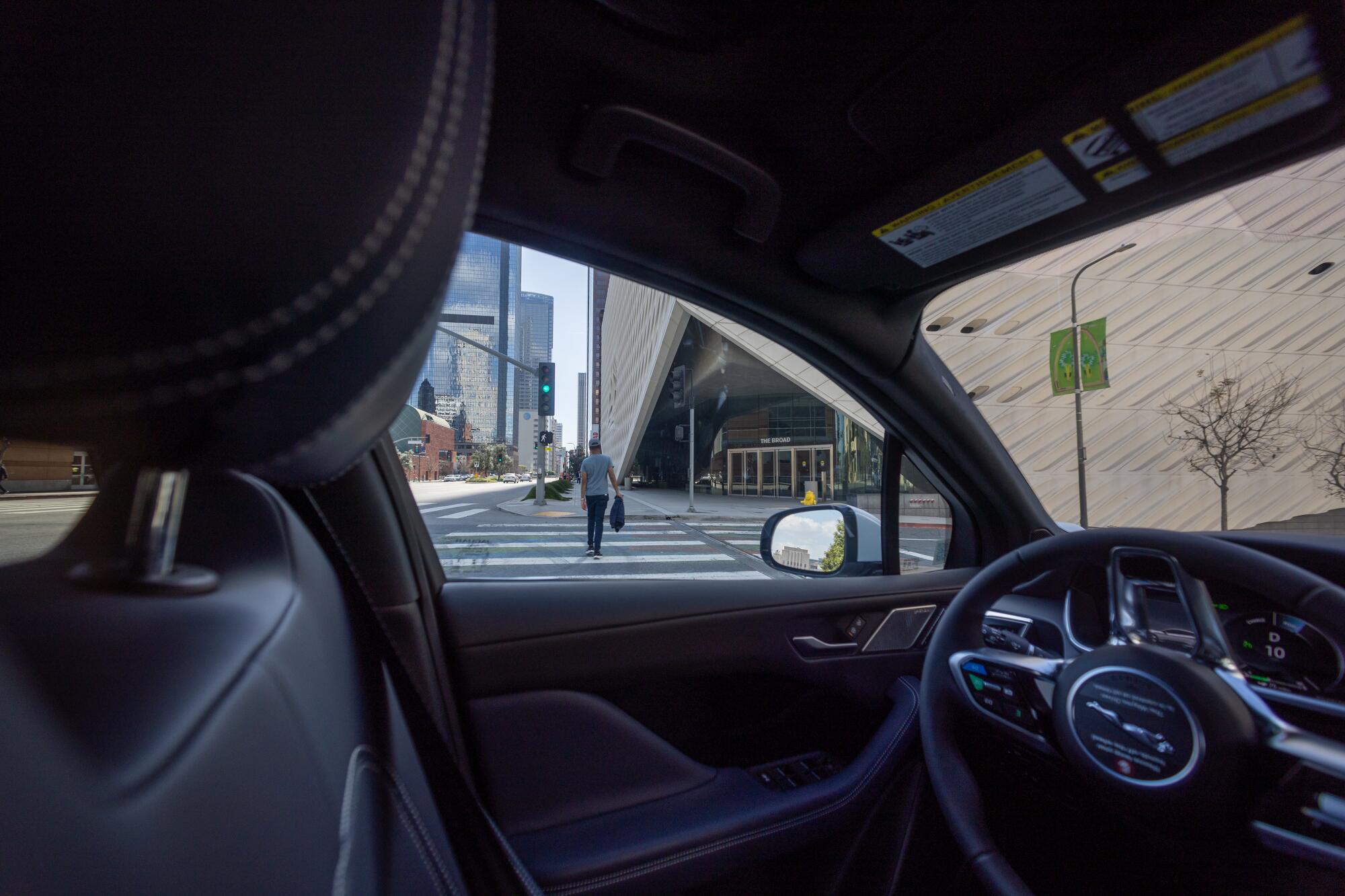 A person in a crosswalk is seen through the driver's side window of a driverless electric vehicle.