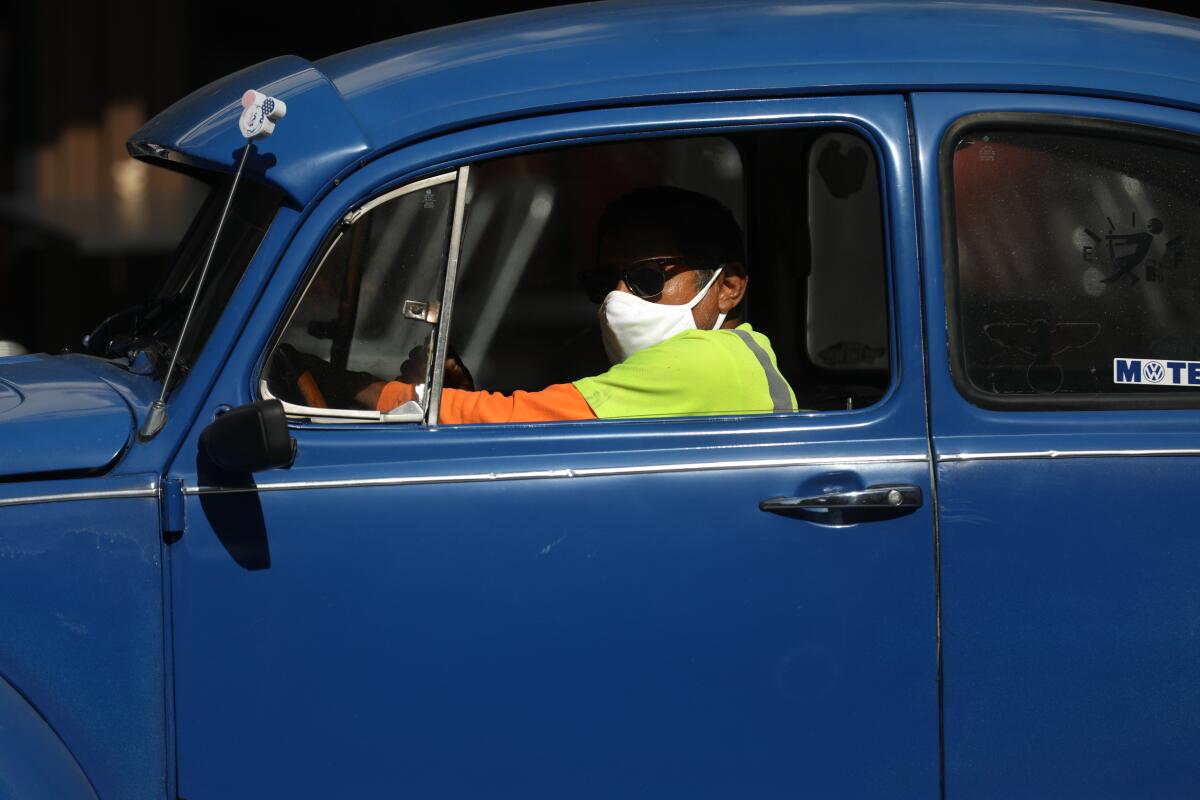 A masked driver in a VW in Old Towne Orange.  In Orange County, where many have refused to wear masks, COVID cases are up.