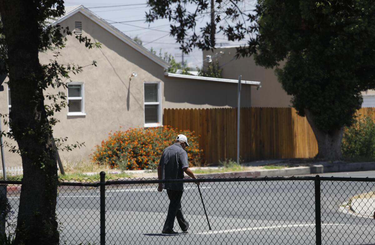 A man with a cane walks through a North Hollywood neighborhood. 