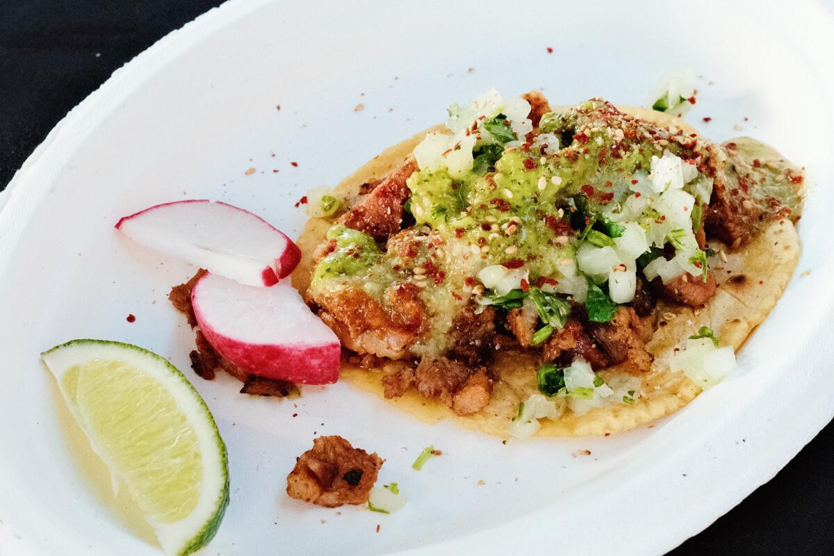 An al pastor taco on a white plate with slices of lime and radish
